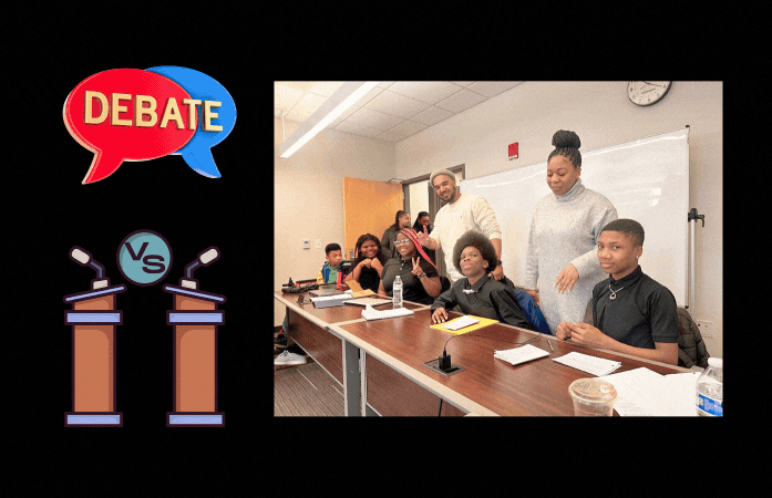  Two adults standing behind 5 students sitting at a table